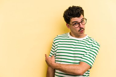 Sarı arka planda izole edilmiş genç beyaz adam gülümsüyor ve boş alanda bir şeyler gösteriyor..