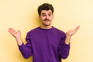 Kafkasyalı genç adam sarı arka planda izole edilmiş. Kafası karışmış ve omuz silkiyor. Kopya alanını tutmak için..