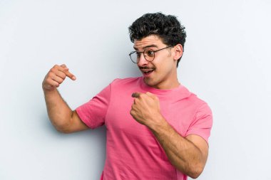 Mavi arka planda izole edilmiş genç beyaz adam parmağını göstererek şaşırdı, geniş bir gülümsemeyle..