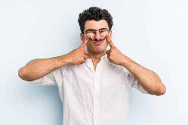 Kafkasyalı genç adam mavi arka planda izole edilmiş iki seçenek arasında şüphe duyuyor.