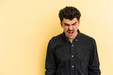 Sarı arka planda izole edilmiş genç beyaz bir adam çok kızgın, öfkeli, hayal kırıklığına uğramış diye bağırıyor..