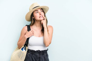 Young caucasian woman holding beach bag isolated on blue background relaxed thinking about something looking at a copy space.