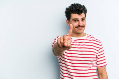 Mavi arka planda izole edilmiş genç beyaz adam bir numarayı parmağıyla gösteriyor..