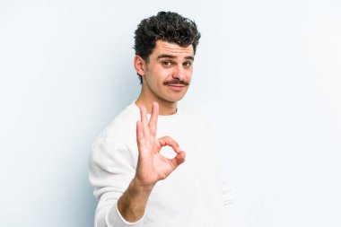 Kafkasyalı genç bir adam mavi arka planda izole edilmiş bir şekilde göz açıp kapayana kadar iyi bir el hareketi yapıyor..