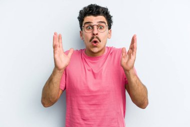 Kafkasyalı genç adam mavi arka planda izole edildi. Şaşırdı ve şok oldu..