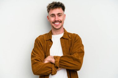 Beyaz arka planda kendini güvende hisseden, kararlılıkla kollarını kavuşturan beyaz tenli genç bir adam..