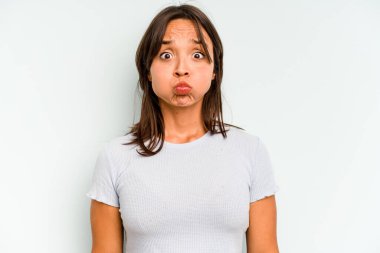 Mavi arka planda izole edilmiş genç İspanyol kadın gülümsüyor ve boş alanda bir şeyler gösteriyor..