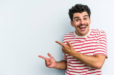 Kafkasyalı genç adam mavi arka planda izole edilmiş. İşaret parmağıyla işaret ettiği için heyecanlı..