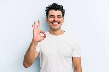 Kafkasyalı genç adam mavi arka planda izole edilmiş neşeli ve kendinden emin..
