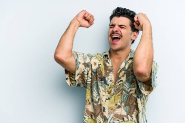 Mavi arka planda izole edilmiş genç beyaz bir adam zaferden sonra yumruğunu kaldırıyor, kazanan konsept..