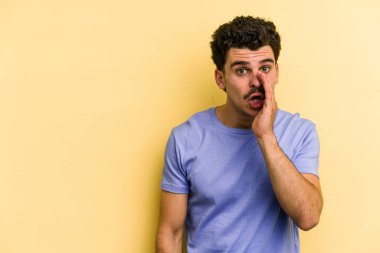 Sarı arka planda izole edilmiş genç beyaz bir adam gizli bir sıcak fren haberi veriyor ve yana bakıyor.