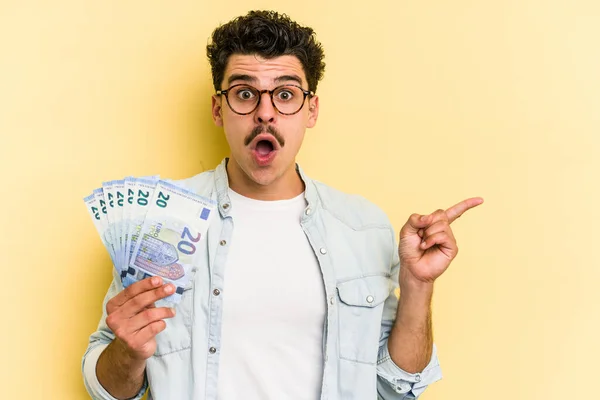 Young Caucasian Man Holding Banknotes Isolated Yellow Background Pointing Side — Stock fotografie