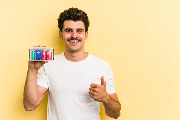 Young Caucasian Man Holding Batteries Isolated Yellow Background Smiling Raising — Stock Fotó