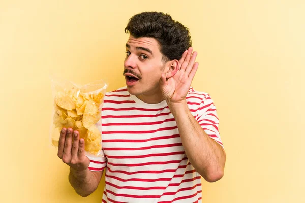 Young Caucasian Man Holding Bag Chips Isolated Yellow Background Trying — Stockfoto