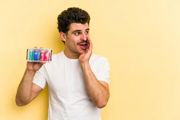 Young Caucasian Man Holding Batteries Isolated Yellow Background Saying Secret — Stock Fotó