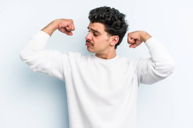 Mavi arka planda izole edilmiş genç beyaz adam güçlü bir hareket sergiliyor kollarıyla, kadınsı gücün sembolü.