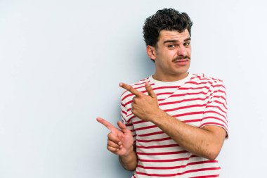 Mavi arka planda izole edilmiş genç beyaz adam işaret parmağıyla fotokopi alanını işaret ederek şok oldu..