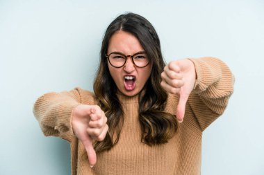Mavi arka planda izole edilmiş genç beyaz kadın baş parmağını aşağı gösteriyor ve hoşlanmadığını ifade ediyor..