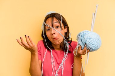 Young hispanic woman holding a ball of wool isolated on yellow background