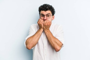 Mavi arka planda izole edilmiş, tırnak yiyen, gergin ve endişeli genç bir beyaz adam..