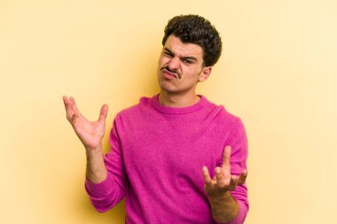 Sarı arka planda izole edilmiş genç beyaz adam sorgulama sırasında omuz silkiyor ve kuşkulanıyor..