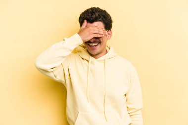 Sarı arka planda izole edilmiş genç beyaz adam elleriyle gözlerini kapatıyor, geniş bir gülümsemeyle bir sürpriz bekliyor..