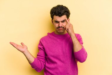 Sarı arka planda izole edilmiş genç beyaz adam işaret parmağıyla hayal kırıklığı jesti yapıyor..