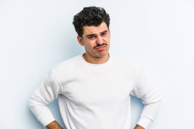 Kafkasyalı genç adam mavi arka planda izole edilmiş üzgün, ciddi yüzlü, mutsuz ve hoşnutsuz..