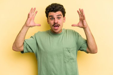 Sarı arka planda izole edilmiş genç beyaz bir adam zaferi ya da başarıyı kutluyor, şaşırıyor ve şok oluyor..