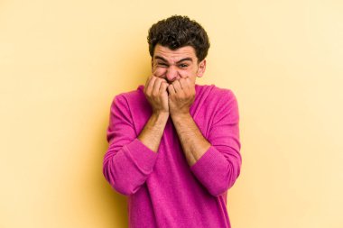 Sarı arka planda izole edilmiş, tırnak yiyen, gergin ve endişeli genç bir beyaz adam..