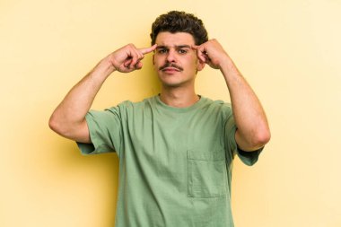 Sarı arka planda izole edilmiş genç beyaz adam bir göreve odaklanmış, işaret parmaklarını işaret ediyor..