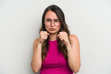 Beyaz arka planda izole edilmiş genç beyaz kadın yumruğunu kameraya gösteriyor, agresif yüz ifadesi var..