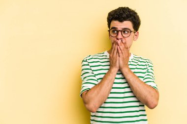 Kafkasyalı genç adam sarı arka planda izole edilmiş. Düşünceli bir şekilde, ağzını eliyle kapatan bir fotokopi odasına bakıyor..