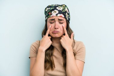 Kafkasyalı genç bir kadın mavi arka planda izole edilmiş, ağlıyor, bir şeyden memnun değil, acı ve kafa karışıklığı konsepti..