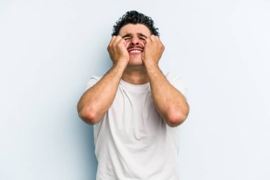 Kafkasyalı genç adam mavi arka planda izole edilmiş, ağlıyor, bir şeyden memnun değil, acı ve kafa karışıklığı konsepti..