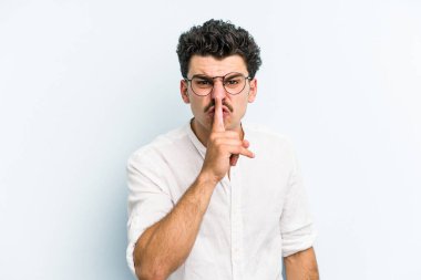 Mavi arka planda izole edilmiş genç beyaz bir adam ya sır saklıyor ya da sessizlik istiyor..