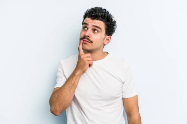 Kafkasyalı genç bir adam mavi arka planda izole edilmiş. Bir strateji planlıyor, bir iş yolu düşünüyor..