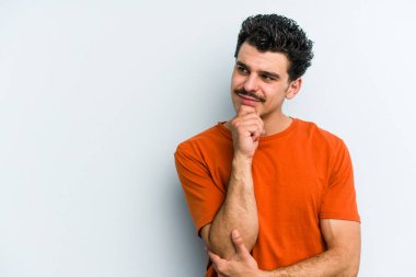 Mavi arka planda izole edilmiş genç beyaz adam rahatlamış bir şeyin fotokopi odasına baktığını düşünüyor..