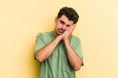 Sarı arka planda izole edilmiş genç beyaz adam esniyor. Ağzı eliyle kapatan yorgun bir hareket sergiliyor..