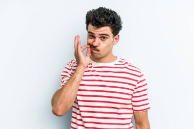 Genç beyaz adam mavi arka planda izole edilmiş ve parmakları dudaklarında bir sır saklıyor..