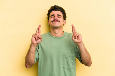 Sarı arka planda izole genç beyaz adam şans dilemek için şans diliyor.