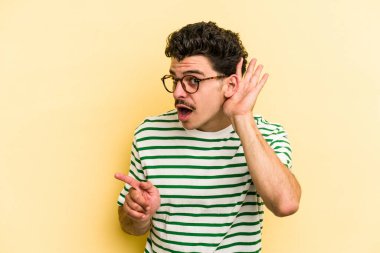 Sarı arka planda izole edilmiş genç beyaz bir adam bir dedikoduyu dinlemeye çalışıyor..