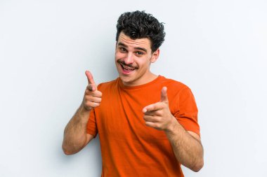 Mavi arka planda izole edilmiş genç beyaz adam parmaklarıyla ön tarafı işaret ediyor..