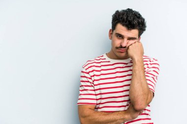 Mavi arka planda izole edilmiş, üzgün ve dalgın hisseden, kopyalama alanına bakan genç beyaz bir adam..