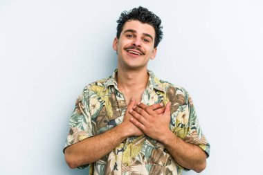 Mavi arka planda izole edilmiş beyaz bir genç, dost bir ifadeye sahip, avuçlarını göğsüne bastırıyor. Aşk konsepti.