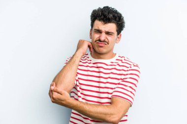 Kafkasyalı genç adam mavi arka planda izole edilmiş dirsek masajı yapıyor, kötü bir hareketin ardından acı çekiyor..