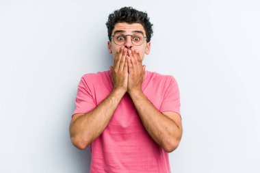 Mavi arka planda izole edilmiş genç beyaz adam elleriyle ağzını kapatırken şok oldu..