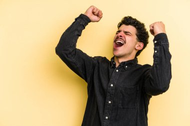 Sarı arka planda izole edilmiş genç beyaz adam zaferden sonra yumruğunu kaldırıyor, kazanan konsept..