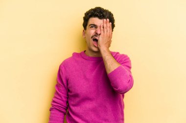 Sarı arka planda izole edilmiş genç beyaz adam yorgun ve uykulu bir şekilde ellerini başının üstünde tutuyor..