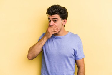 Sarı arka planda izole edilmiş genç beyaz adam elleri endişeli bir şekilde ağzı örtüyor..